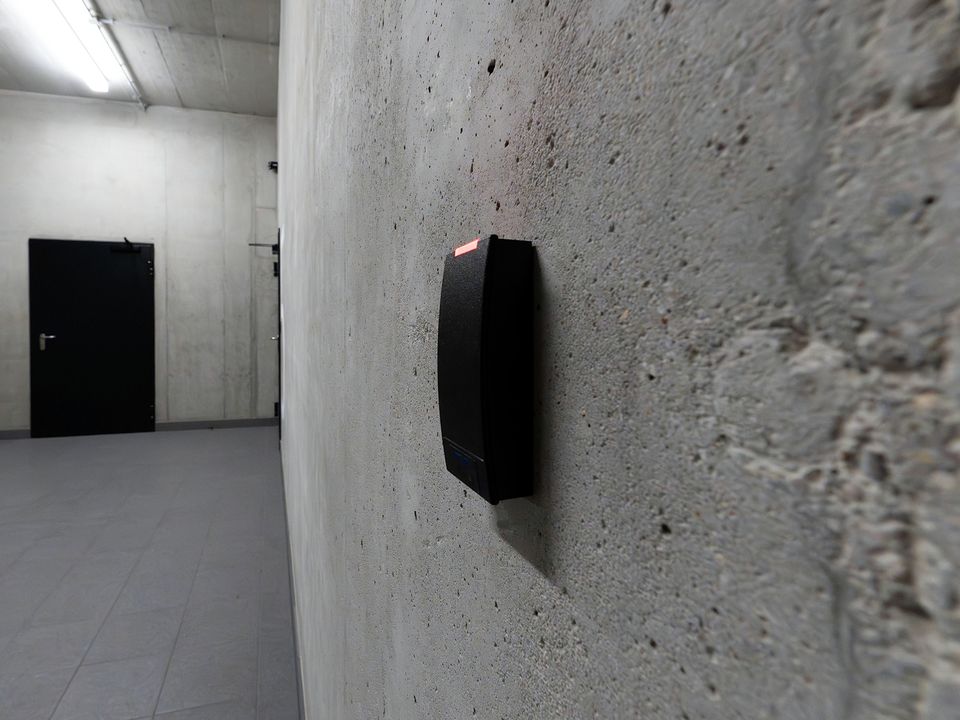 Lecteur de badge noir fixé sur un mur en béton, dans un couloir
